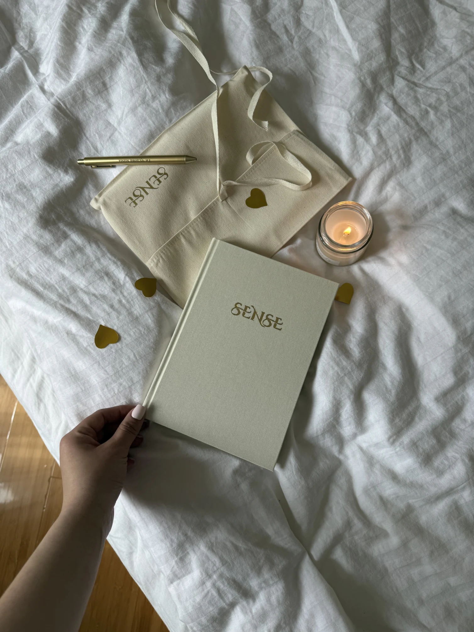 Cream SENSE Baby Book, a fabric envelope and a gold pen on a bed