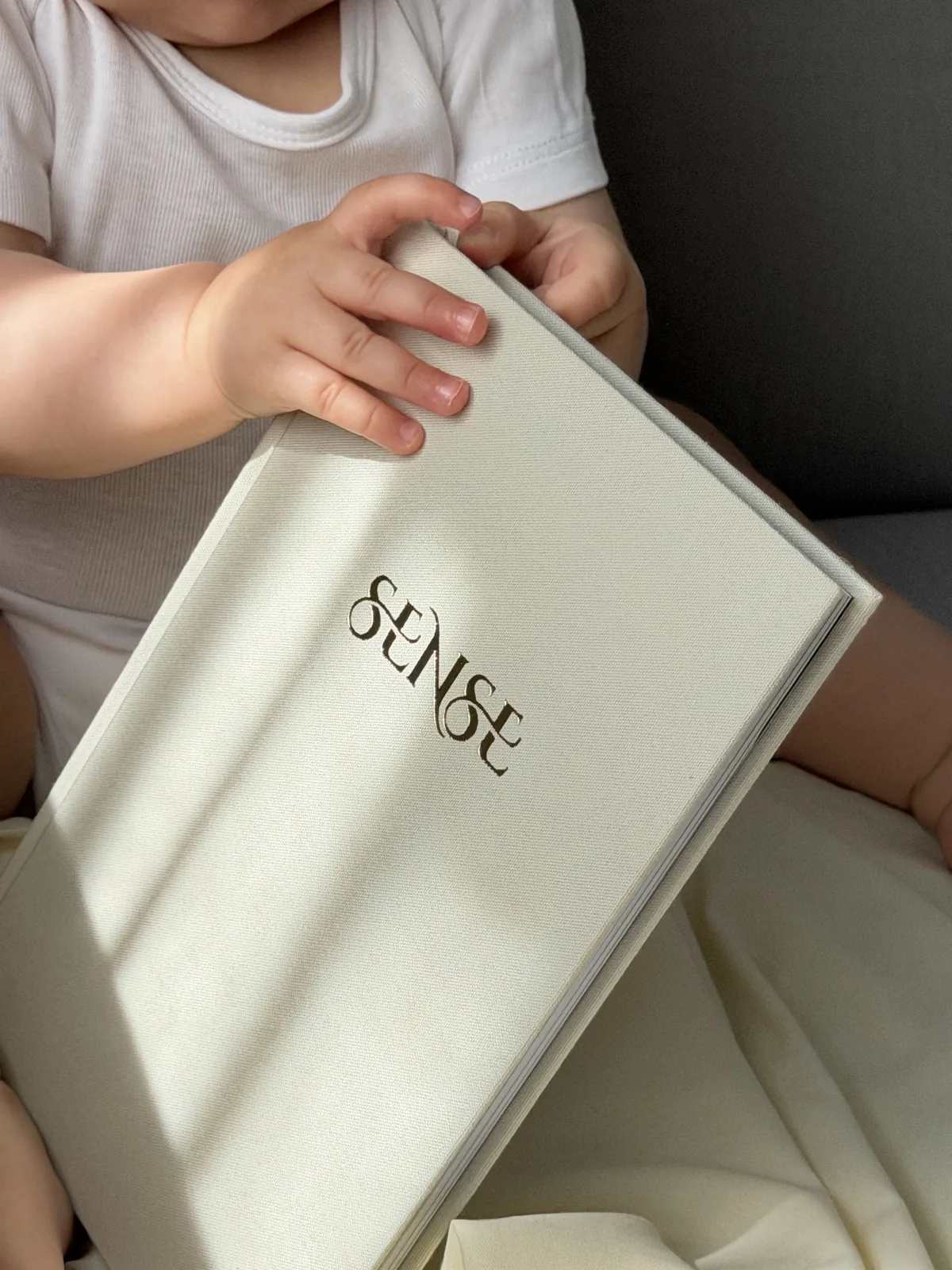 Cream SENSE baby memory book in a baby’s hands