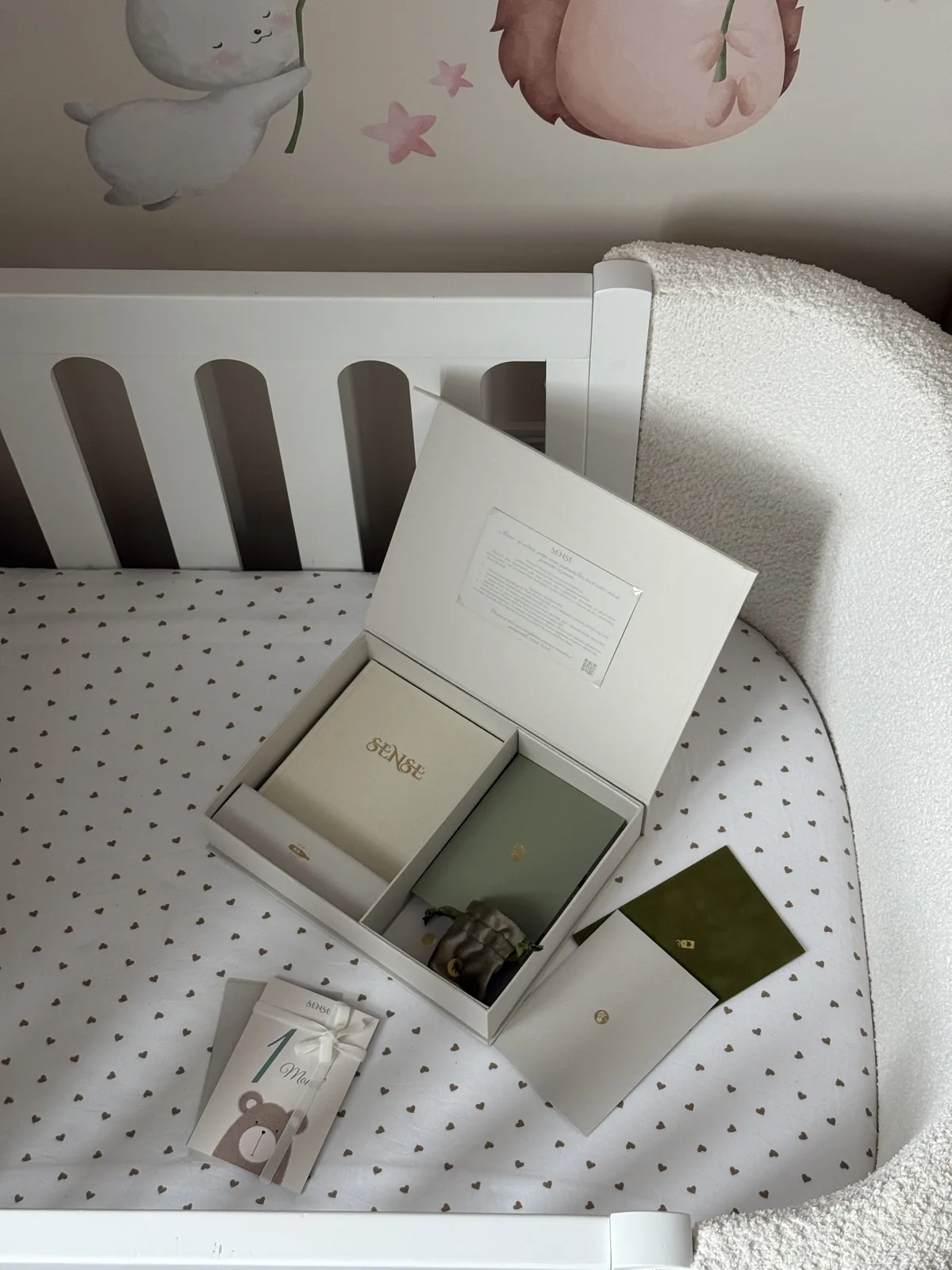 Cream SENSE baby memory box with its contents in a cot